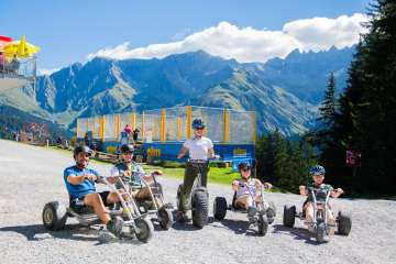 Group of young adults riding mountain carts and scooters downhill in sunny Elm.