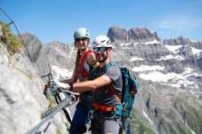 Two people wearing helmets and climbing gear on the via ferrata above Braunwald in the Glarus Alps