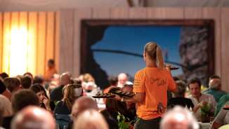 Woman serving food in an orange Tshirt, that the helpers at ESAF wore, in a tent full of visitors of esaf