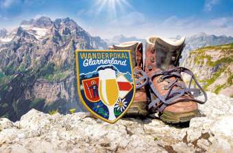 Hiking boots and the Glarnerland Hiking Trophy emblem set against a stunning mountain backdrop.
