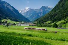 A regional train travels through a green valley near Diesbach, GL, with mountains in the background