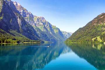 Lake Klöntal shimmering in deep blue, surrounded by steep cliffs and lush forests in the Glarus region.