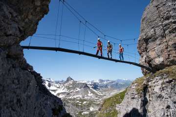 Three climbers crossing a suspension bridge on a via ferrata near Braunwald in the Swiss Alps