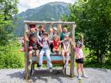 Kindergruppe auf einer Holzinstallation am Spiele- und Erlebnisweg in Braunwald vor Bergkulisse