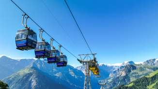 Blue Braunwald gondolas floating above green slopes with a panoramic view of the Alps.