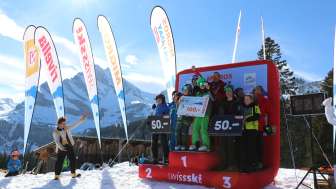 The top three winners of the race at the migros ski day are on the podest with the Ortstock in the background and clown Ischa on the side.