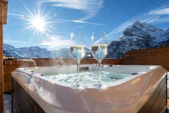 Two champagne glasses on the edge of a steaming outdoor hot tub overlooking the Alps.