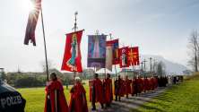 A line of people in red capes carrying ornate religious banners across a field.