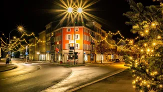 A nighttime street scene in Glarus featuring hanging string lights and a brightly lit orange building at a junction.