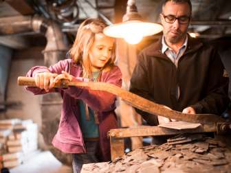 Child and adult working together on an old cutting machine in the Slate Factory Elm.
